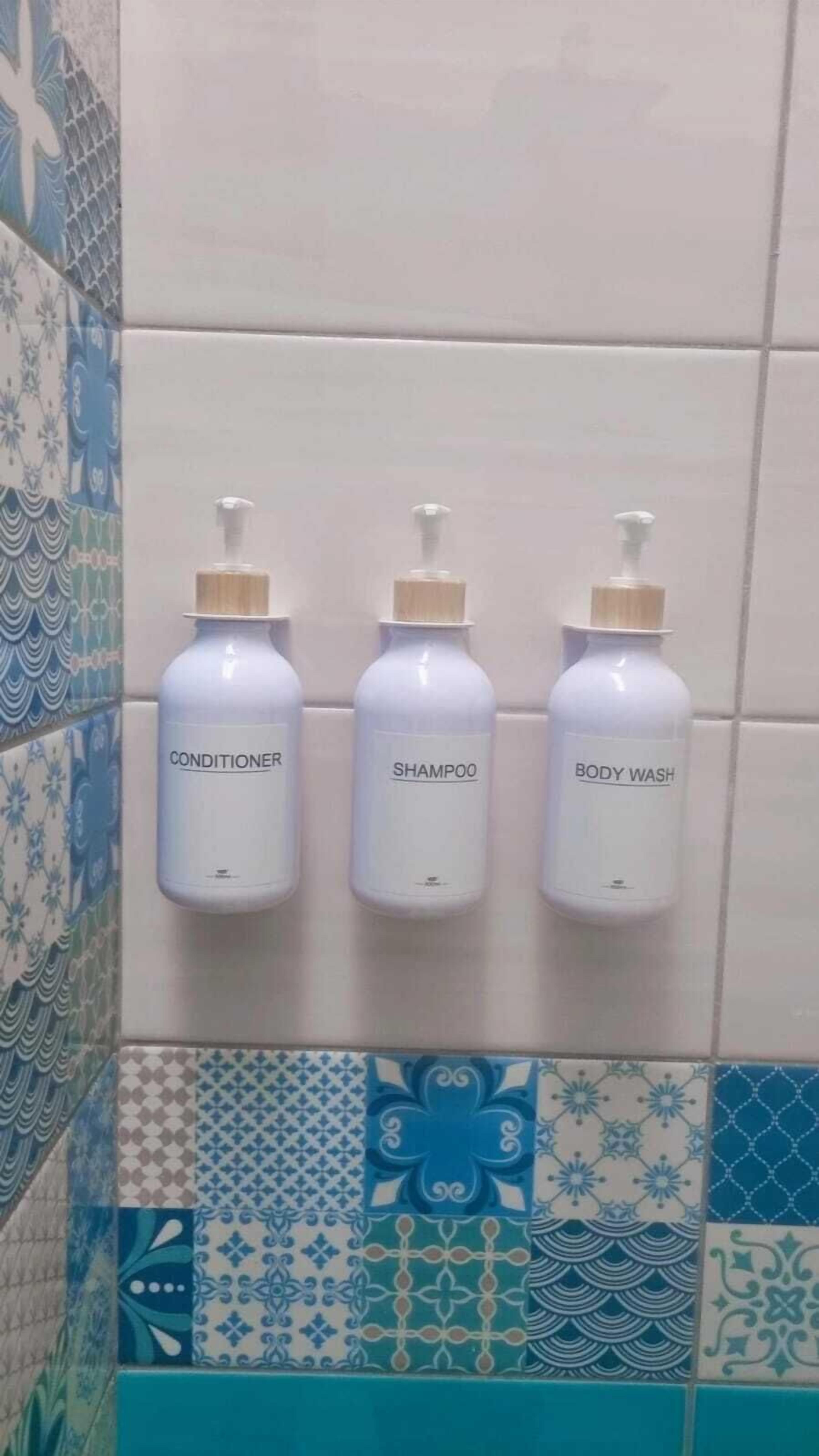 Three bottles of conditioner, shampoo, and body wash mounted on a tiled wall.