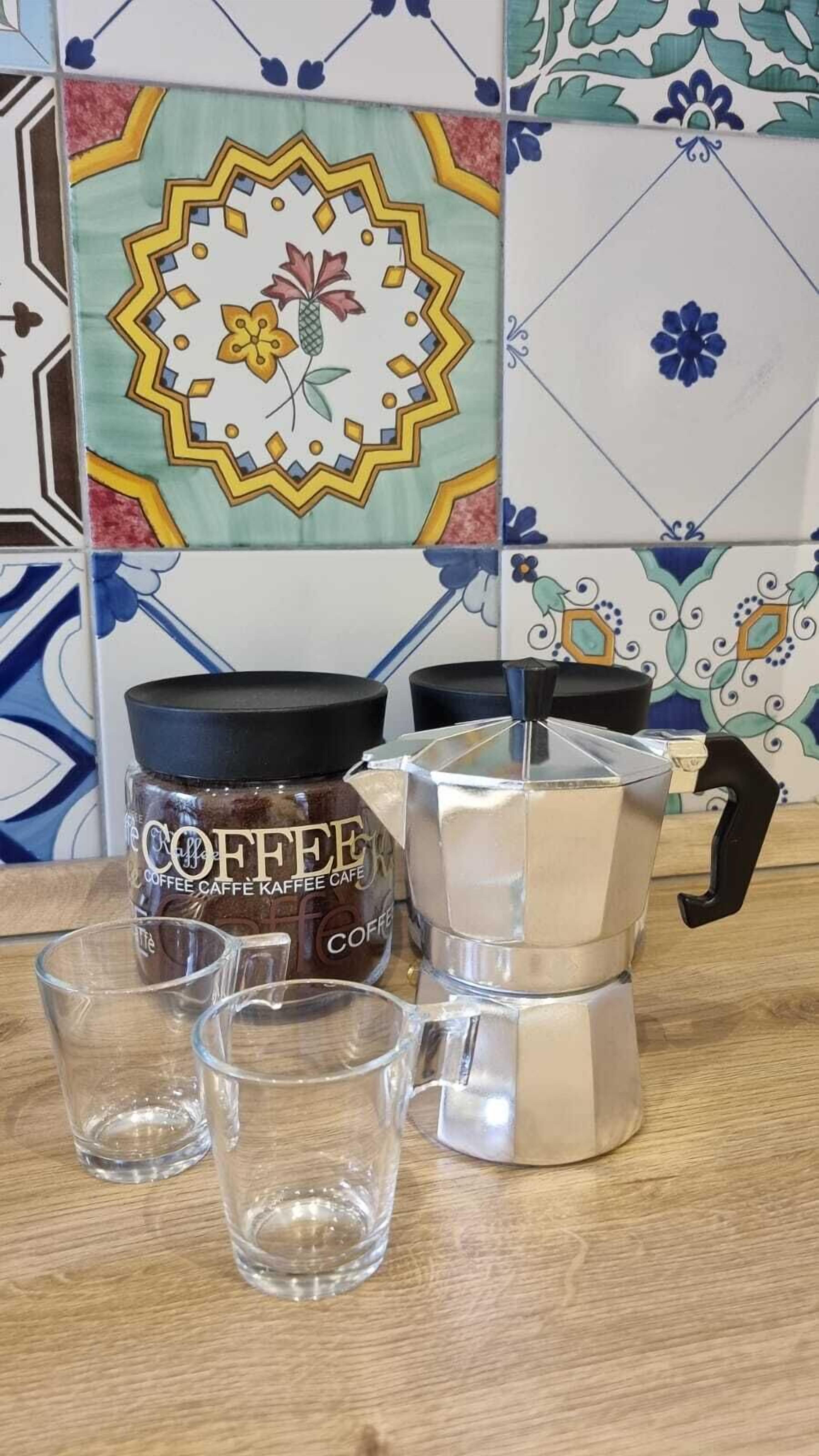 A coffee maker, a jar of coffee, and two empty glasses on a wooden table.