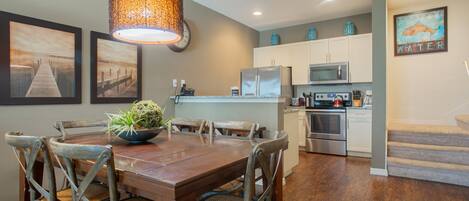 A dining area with a wooden table and chairs, a hanging light fixture, and artwork on the walls.