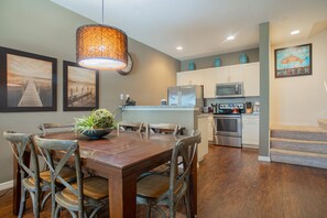 A dining area with a wooden table and chairs, a hanging light fixture, and artwork on the walls. - Spacious 3-bedroom townhome in Kissimmee, perfect for family getaways! (Kissimmee)