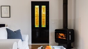 A cozy living room with a white sofa, a coffee table with books, a black wood-burning stove, and a door with stained glass panels. - A Cottage In Richmond (Richmond)