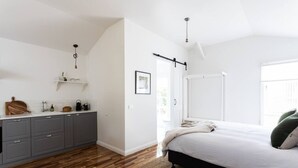 A bedroom with a bed, a wooden floor, a kitchen area with cabinets, and a window. - A Cottage In Richmond (Richmond)