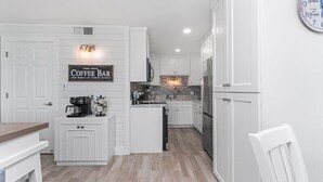 A kitchen with white cabinetry, a coffee bar sign, a clock, and a stone backsplash. - Summit Gulf Front Unit 421 | 4th Floor (Panama City Beach)