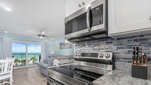A modern kitchen with stainless steel appliances, a large island, and a view of the ocean. - Summit Gulf Front Unit 421 | 4th Floor (Panama City Beach)