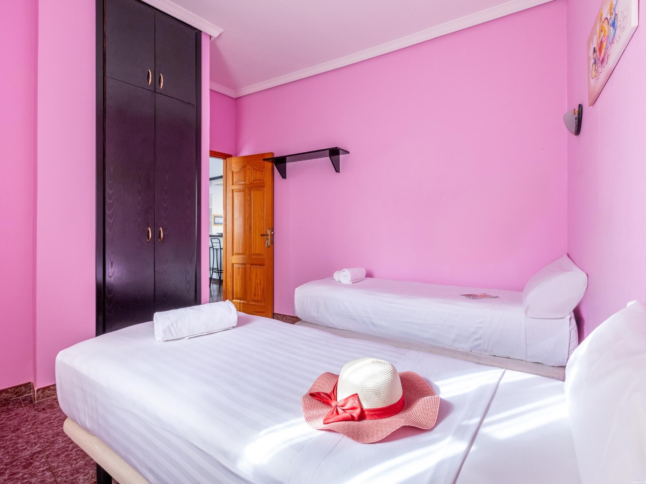 A room with two beds, a wardrobe, and a door leading to a balcony.