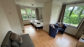 A room with a sofa, two beds, a chair, and large windows with a view of greenery. - B&B Zwiep (Lochem)