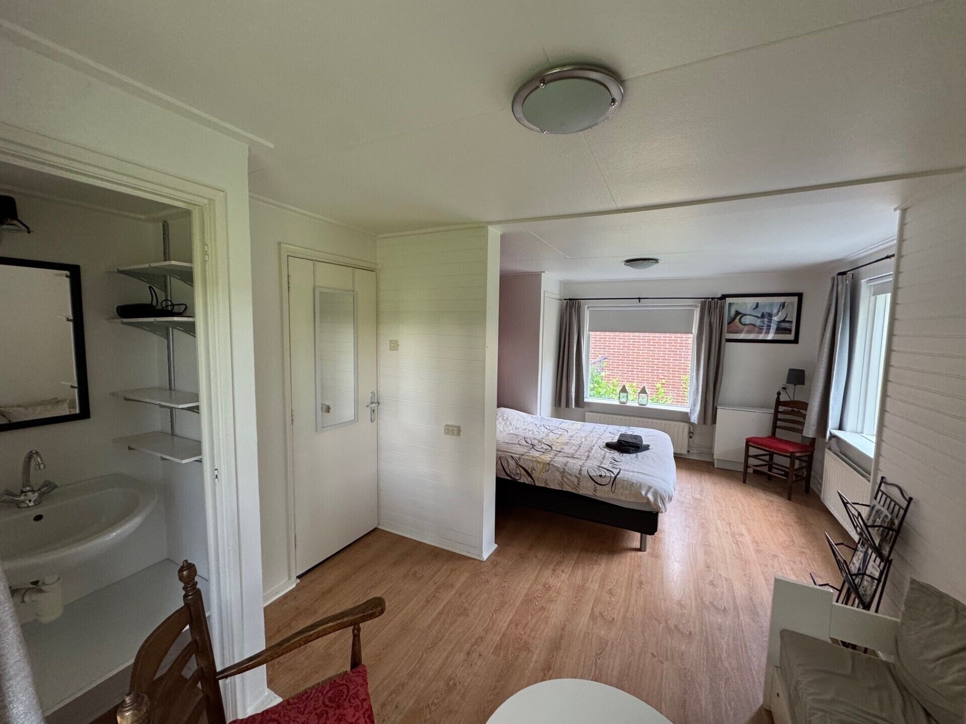 Een slaapkamer met een bed, een raam met gordijnen, een radiator en een stoel.