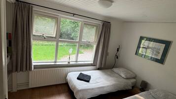 A room with two beds, a window with curtains, a radiator, and a framed picture on the wall.