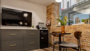 Cocina compacta con un refrigerador negro moderno, un televisor de pantalla plana y una mesa de comedor de madera con dos sillas.