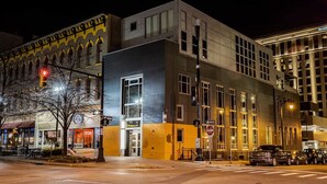 Un edificio moderno con una entrada amplia, un letrero visible con la dirección y una señal de tráfico que indica 'One Way'.