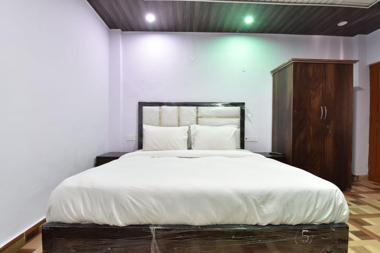 A neatly made bed with white linens, a wooden headboard, and a dark-colored nightstand beside it.