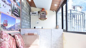 Un espace d’accueil d’hôtel comprenant un canapé, un climatiseur fixé au mur et une fenêtre donnant sur une montagne et un bâtiment.
