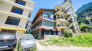 Un hôtel à plusieurs étages doté de balcons, une enseigne bien visible indiquant « Top Hotels », et une voiture garée devant.