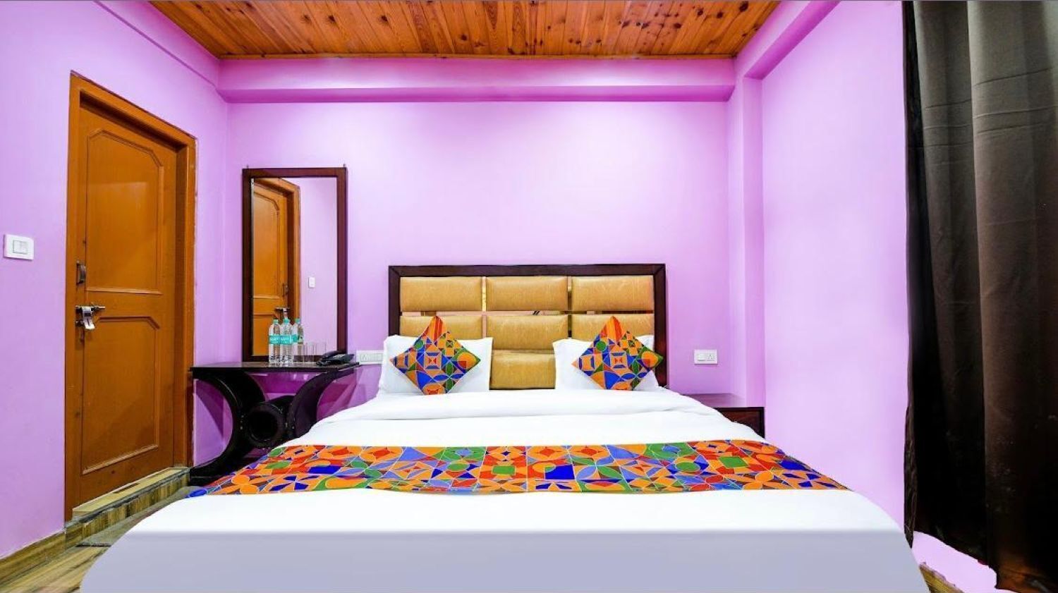 Une chambre d’hôtel avec un plafond en bois, un lit recouvert d’une courtepointe aux motifs géométriques colorés et une tête de lit au motif matelassé.