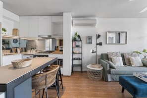 Una cocina moderna con una isla central, un comedor con sillas, un sofá y una pequeña mesita auxiliar.