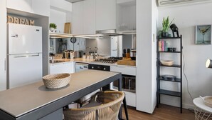 Una cucina moderna con mobili bianchi, un'area pranzo con tavolo e sedie, e una libreria con libri e oggetti decorativi.