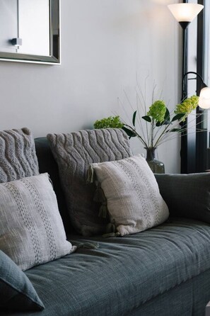 Un sofá gris con almohadones de punto y un jarrón con plantas verdes.