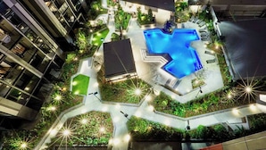 Un edificio moderno con piscina, circondato da vegetazione e zone relax all'aperto.