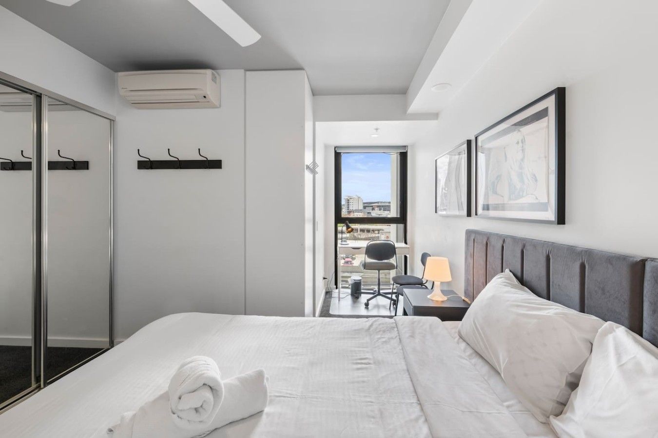 Una camera d'albergo con un letto, una scrivania con una lampada, una sedia, una finestra vista e un armadio.