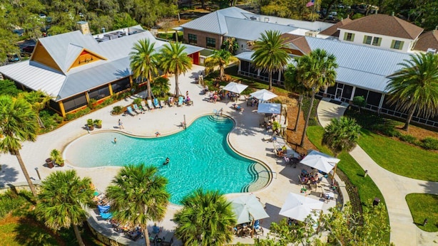 Luftaufnahme eines Resorts mit einem zentral gelegenen Schwimmbad, umgeben von Palmen und Liegebereichen.