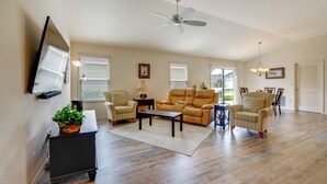 Ein großzügiges Wohnzimmer mit Deckenventilator, Ledersofa, Sesseln, einem Couchtisch und einem an der Wand befestigten Fernseher.