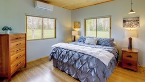 A bedroom with a wooden ceiling, a bed with a blue duvet, two bedside lamps, a wooden nightstand, and a dresser. - Fish, Hike & More! Home w/ Views in Stevensville (Stevensville)