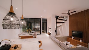 A modern living room with a dining area, a built-in TV, and a staircase. - 3-bedroom Aquamarine villa in awesome Bali with Private Pool (Bali)