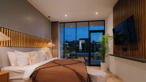 A modern bedroom with a large bed, a TV mounted on the wall, and a view of the outdoors through a glass door. - 3-bedroom Aquamarine villa in awesome Bali with Private Pool (Bali)