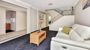 A modern interior with a white sofa, a wicker side table, and a staircase. - Hidden Horizon (Nords Wharf)