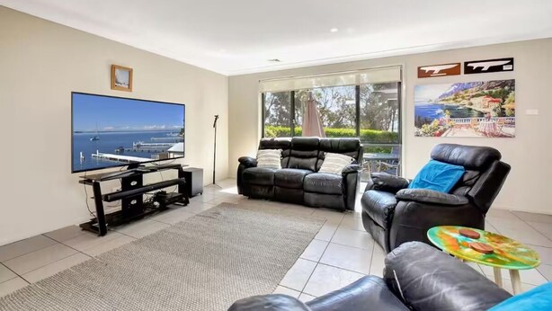 A living room with a large flat-screen TV, two black leather sofas, a small round table, and a view of the sea through large windows. - Hidden Horizon (Nords Wharf)