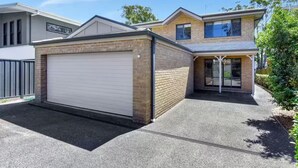 A modern two-story house with a garage, brick exterior, and a covered driveway. - Hidden Horizon (Nords Wharf)