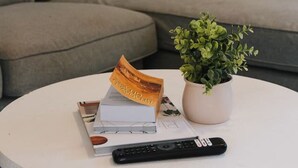 Een ronde witte salontafel met een afstandsbediening, een boek en een bloempot.