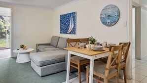 Een moderne woonkamer met een grijze bank, een houten eettafel voor vier personen en een ronde wandklok.