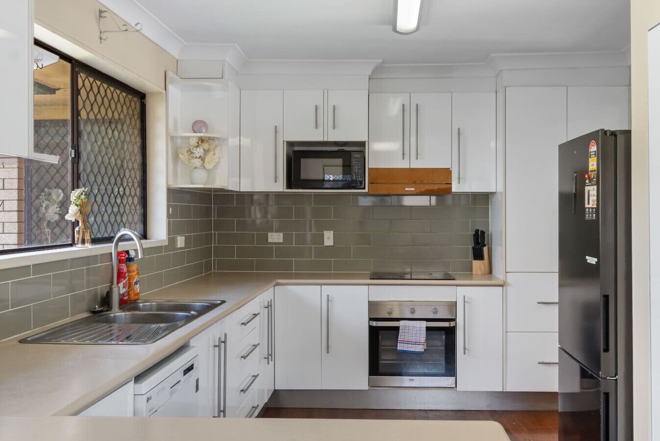 Eine moderne Küche mit weißen Schränken, einem Edelstahlbackofen, einer Mikrowelle und einem Kühlschrank.