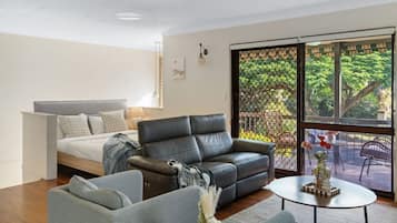 A modern living room with a bed, a leather sofa, a grey armchair, and a coffee table.