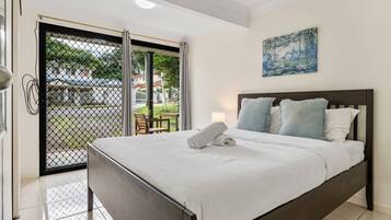 A hotel room with a bed, a painting on the wall, and a view through a glass door.