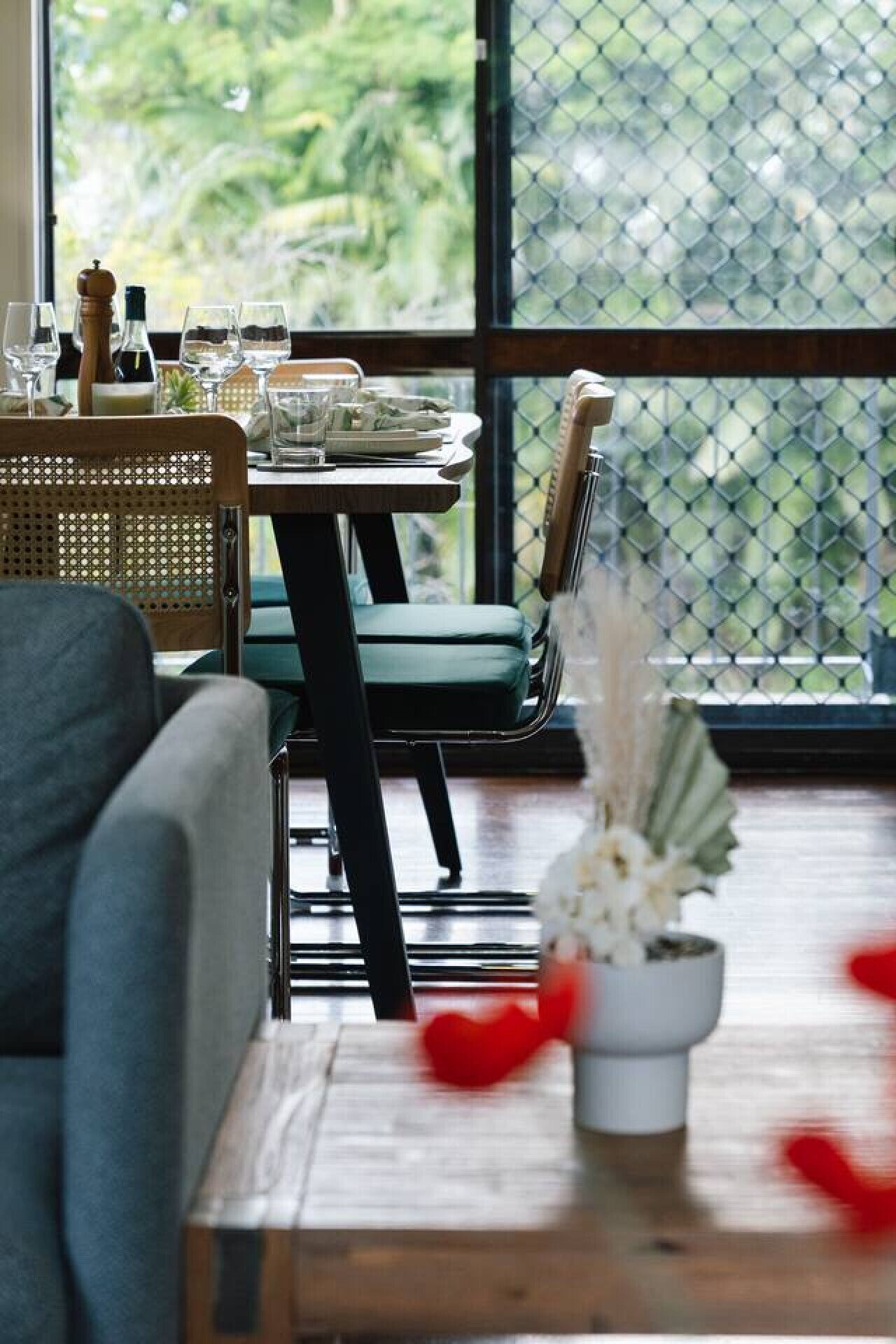 A dining area with a table set for two, a sofa, and a view through a glass door.