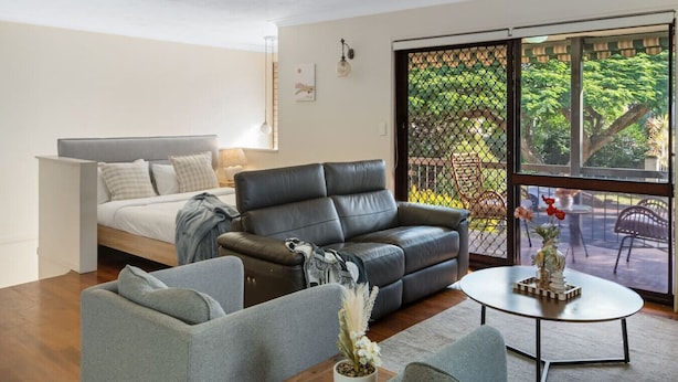 A modern living room with a bed, a leather sofa, a grey armchair, and a coffee table. - Unbeatable Value | Group/Family | Roomy/Convenient (Robertson)