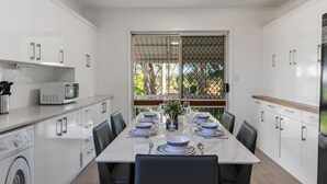 A modern kitchen with white cabinets, a microwave, and a dining table set for six with blue and white plates. - High-Value 4Beds | Workspace | Near Mall & Highway (Macgregor)