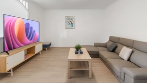 A modern living room with a flat-screen TV, a wooden coffee table, a beige sofa, and a small side table with a vase and candles. - High-Value 4Beds | Workspace | Near Mall & Highway (Macgregor)
