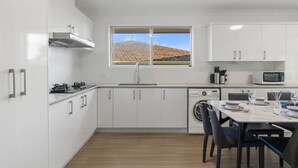 A modern kitchen with white cabinets, a stainless steel sink, a dishwasher, and a window with a view of a hill. - High-Value 4Beds | Workspace | Near Mall & Highway (Macgregor)
