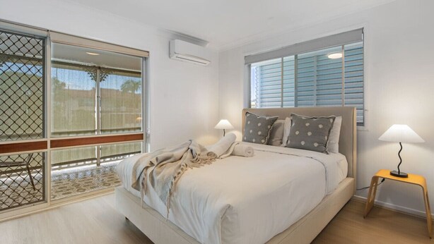 A modern bedroom with a large bed, two bedside lamps, and a view through a sliding glass door. - High-Value 4Beds | Workspace | Near Mall & Highway (Macgregor)