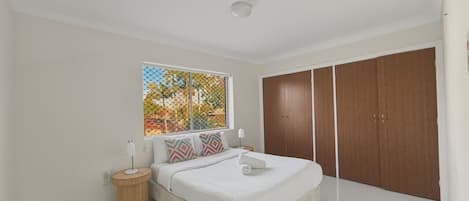 Ein Schlafzimmer mit Bett, Nachttischen, einem Fenster mit Aussicht und einem Kleiderschrank.