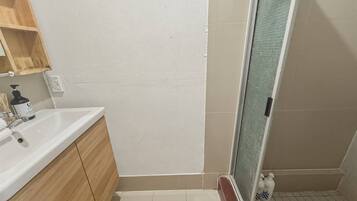 Une salle de bain avec un lavabo blanc, des meubles en bois, un espace douche et un sol carrelé.