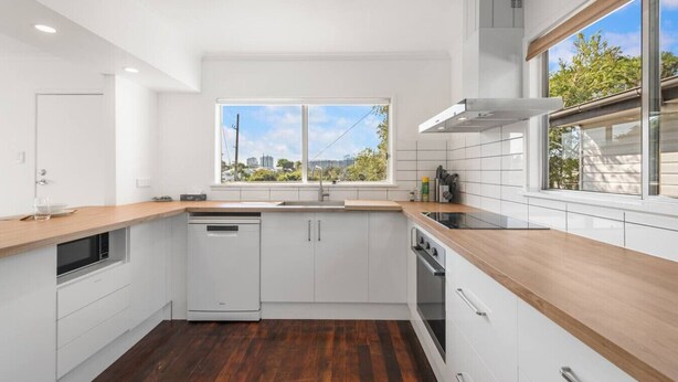 A modern kitchen with white cabinets, a wooden countertop, a dishwasher, an oven, and a window providing a view of the outdoors. - 3Beds Value & Comfort Stay | Airport, CBD & Cafes (Bulimba)