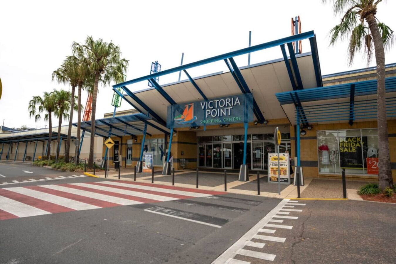 Un centro commerciale Victoria Point con ingresso coperto, palme e un attraversamento pedonale.