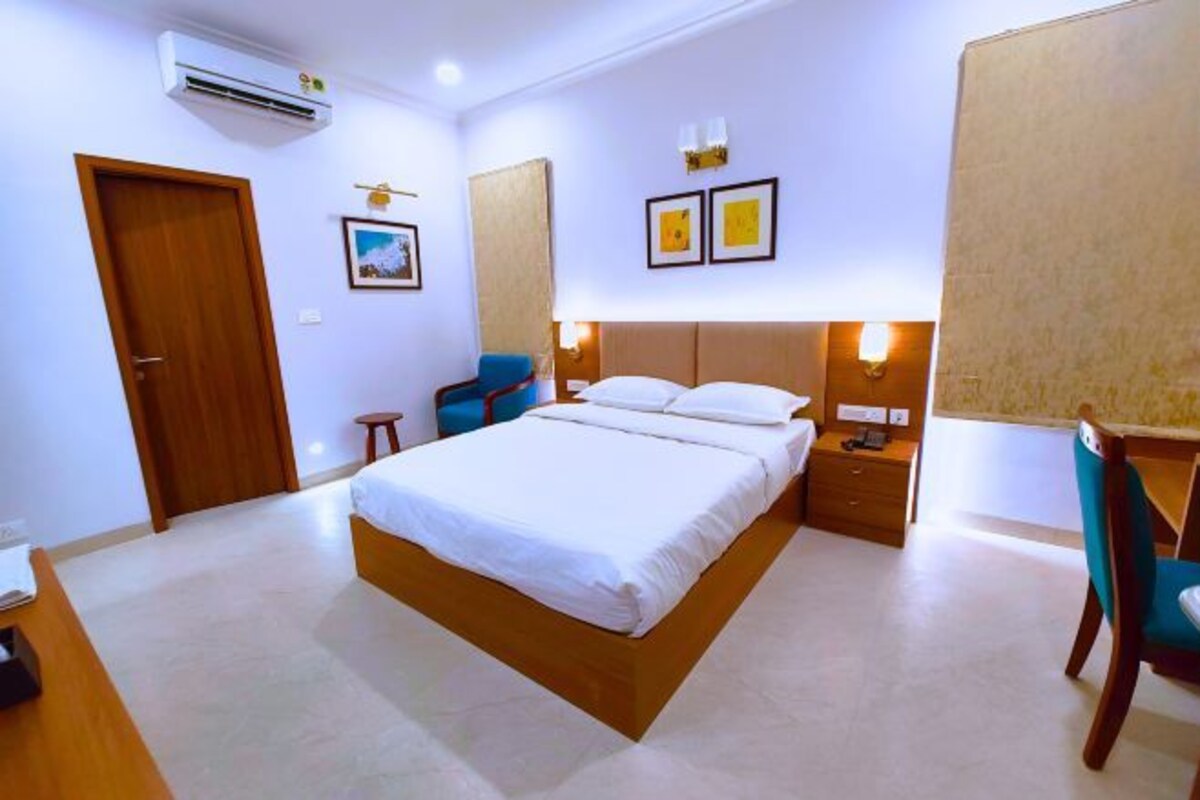 A hotel room with a large bed, a desk, a chair, a wardrobe, and an air conditioning unit.