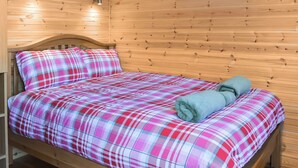 Una habitación de cabaña de madera con una cama, un cuadro colgado en la pared y dos apliques.