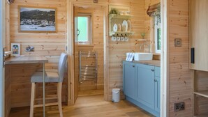 Interior de una cabaña de madera con cocina, comedor y un baño pequeño.