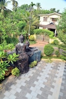 A statue of a seated figure with a child, surrounded by greenery and a paved area.